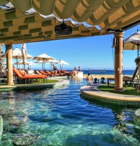 une piscine sur une plage avec des gens assis sur des bancs dans l'établissement Beach resort suite, à Cabo San Lucas