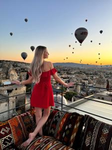 a woman in a red dress standing on a ledge with hot air balloons at Hira Cave Hotel in Göreme