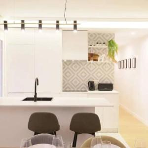 een keuken met witte kasten en een aanrecht met stoelen bij GuestReady - Un Moderno Apartamento a un Paso de la Plaza Mayor in Madrid +6 foto's