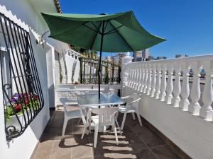 a table and chairs on a balcony with a green umbrella at House totally refurbished in 2024, terrace in front of the sea, 1 min walk to the beach, aircon, wifi in Alicante