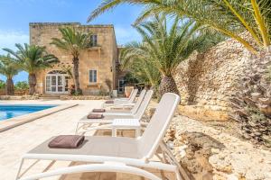 a row of white lounge chairs next to a swimming pool at Sinjura Holiday Home in Xagħra
