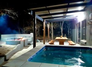 a swimming pool in a backyard at night with a table and bench at Maningwe in Marloth Park