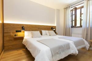 Un dormitorio con una gran cama blanca con cabecero de madera. en El Roble by BeValle, en El Pueyo de Jaca