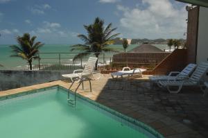 a swimming pool with chairs and the ocean in the background at Costeira Praia 103 in Natal