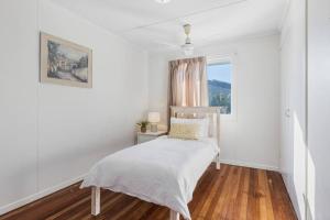 una camera da letto bianca con un letto e una finestra di Warm and Cozy Cottage House a Gympie