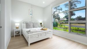 a white bedroom with a bed and large windows at Elliniko in Callala Beach