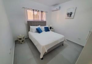 a white bedroom with a bed with blue pillows at Newly Built Beautiful 2BR House With Yard in Punta Cana