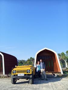 a man and a woman standing next to a yellow jeep at Indah Damai Cottages in Sidomukti
