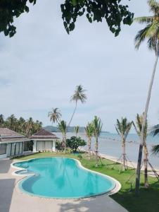 a swimming pool with palm trees and the ocean at Baan Tasha in Laem Sor