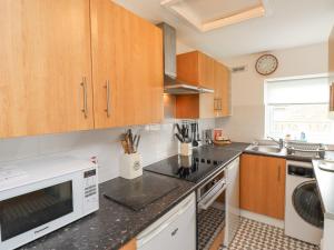 a kitchen with wooden cabinets and a white microwave at Bedwine Cottage in Beadnell