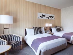 a hotel room with two beds and a chair at Hotel Nikko Narita in Narita