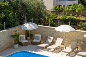two umbrellas and chairs next to a swimming pool at Apartments & rooms Stella Adriatica in Murter