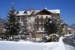 a large building in the snow with trees and a fence at Hotel alle Rose in Cavedago