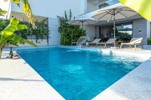 a pool with an umbrella and chairs and a house at Luxury White Sails Villas with a Multi Sport Court and Sea View in Pinezici