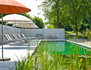uma piscina com guarda-sol, cadeiras e mesas em Biohotel Pausnhof em Sankt Oswald