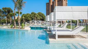 a swimming pool with white lounge chairs and a bridge at Benidorm Beach, Grupo AMI in Benidorm