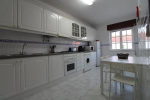 a kitchen with white cabinets and a sink and a table at Casa Cor-de-Rosa in Vila Nova de Milfontes