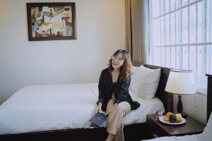 a woman sitting on a bed with a book at Joi Hospitality - Central in Vung Tau