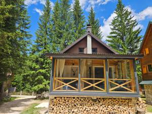 a small house with glass doors and a pile of wood at Black Lake Chalet-300m from Black Lake,Durmitor in Žabljak
