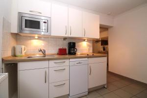 eine Küche mit weißen Schränken und einer Spüle und einer Mikrowelle in der Unterkunft Ferienanlage Dröse, Haus 8a - Fewo 7 rolli-gerecht in Fulgen