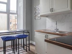 a kitchen with white cabinets and a sink and stools at Pass the Keys West End Cosy Pop of Colour in Glasgow