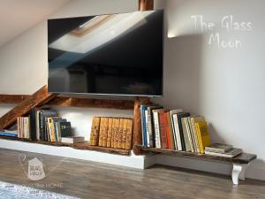 a tv on a wall with books on a shelf at Пространства за гости Синият час - апартамент The Glass Moon in Ruse