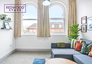 a living room with a blue couch and two windows at Comfortable and Homely 1-Bedroom 1-Bathroom Serviced Apartment with Free Parking, Free WiFi By Redwood Stays in Farnborough
