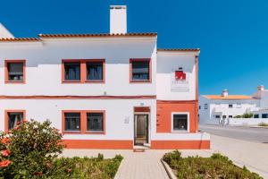 a large white building with red windows on a street at Casa da Praia in Zambujeira do Mar