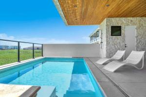 a swimming pool with two white chairs next to a building at Sandbox in Oak Island