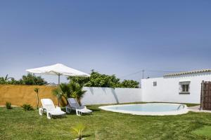 une cour avec deux chaises, un parasol et une piscine dans l'établissement Casa el mirlo, à Conil de la Frontera