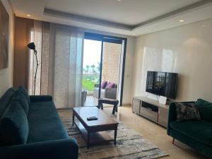 a living room with a couch and a flat screen tv at Plage des Nations Prestigia Vue sur mer in Sidi Bouqnadel