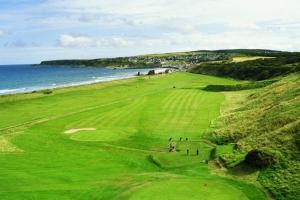 a green golf course with the ocean in the background at Grant Arms Hotel in Cullen