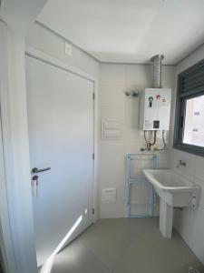 a white bathroom with a sink and a door at Guaruja Terrazza Ap de Alto Padrão Enseada in Guarujá