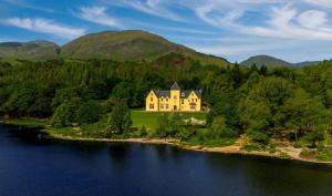 a large yellow house on an island in the water at Glenfinnan House Hotel in Glenfinnan
