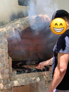 a man wearing a smiley facehat standing next to a brick oven at Villa au coeur de la nature in Menaceur