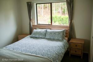 a bedroom with a bed with a window and pillows at Mill Creek Cottage in Coroglen
