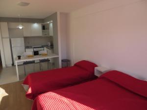 a bedroom with two red beds and a kitchen at Studio en Ovidio Lagos in Rosario