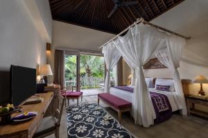 a bedroom with a canopy bed and a desk at Pramana Watu Kurung in Ubud