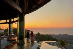 a couple standing on the balcony of a building at sunset at Renaissance Bali Uluwatu Resort & Spa in Uluwatu