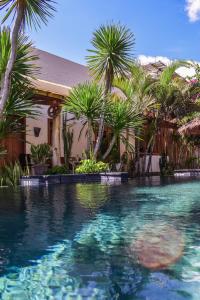 a swimming pool with palm trees in front of a house at Iron Rose Villa with garden & pool Kuta Lombok in Kuta Lombok
