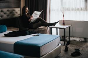 a woman sitting on a couch reading a newspaper at Business Hotel Plovdiv - Central Location in Plovdiv