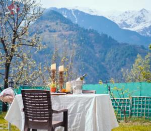 a table and chairs with a table and mountains in the background at The Kailasha Homestay in Nagar