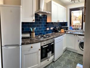 una cocina con armarios blancos y azulejos azules en Aultnagar, en Kirkton of Largo