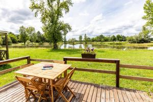 a wooden deck with a table and chairs and a pond at L'héberge du lac d'Isachris mh4 in Queyrac