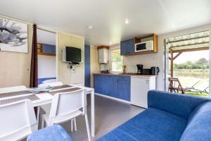 a living room with a blue couch and a kitchen at L'héberge du lac d'Isachris mh6 in Queyrac
