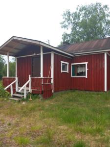 a red house with a porch and a yard at Rustic Old Lakeside Cottage at Sevettijärvi in Sevettijärvi