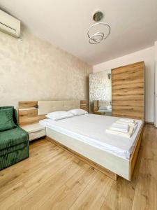 a bedroom with a large bed and a green chair at Апартамент Tiana in Tsarevo