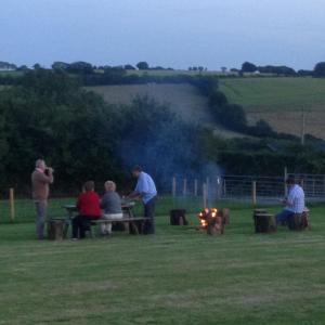 a group of people sitting around a fire in a field at Headgate Farm Camp Site - Pitches Only - Bring your own tent or van in South Molton