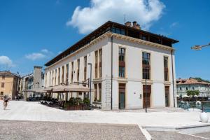 a large white building with an umbrella on a street at C House Rooms Lake in Peschiera del Garda