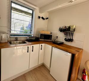 a kitchen with white cabinets and a sink and a microwave at Turtle Cabin in Papamoa +9 photos